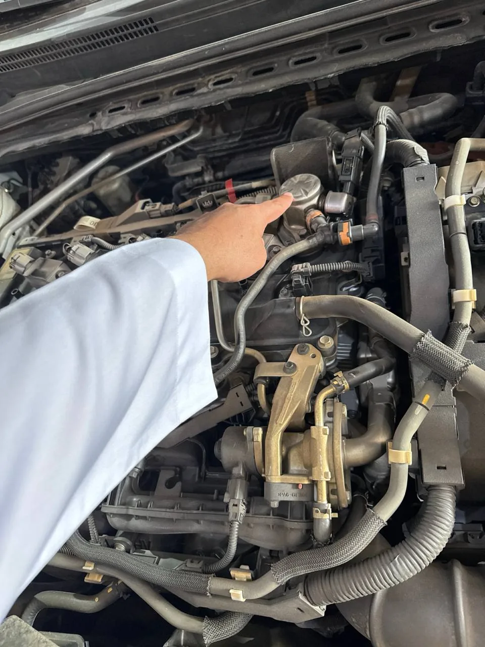 مالك يشير بإصبعه إلى طرمبة الضغط العالي فوق مكينة كامري هايبرد 2019 والكبوت مفتوح